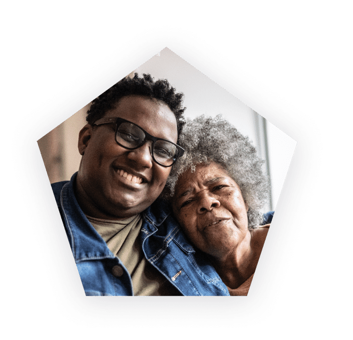 Smiling man wearing glasses hugging an older woman.